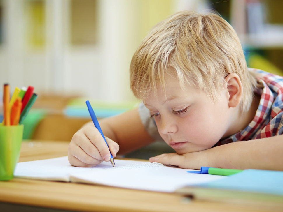 Junge sitzt gelangweilt über den Schularbeiten
