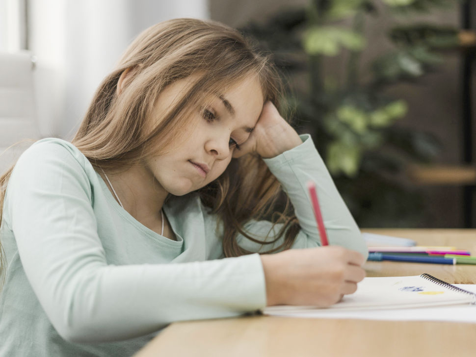 Mädchen sitzt schlecht gelaunt über den Schularbeiten